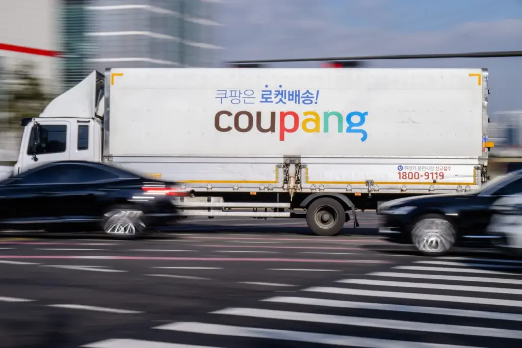 A delivery truck of South Korean e-commerce giant Coupang is driven along a road in Seoul on December 9, 2025. South Korean police raided the Seoul headquarters of e-commerce giant Coupang on December 9, over a recent data leak believed to have affected almost two-thirds of the country's population. (Photo by ANTHONY WALLACE / AFP via Getty Images)